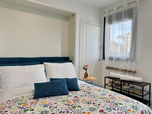 Camera da letto moderna e luminosa in Aurora View Resort con testata blu, biancheria floreale, balcone con vista mare e design contemporaneo