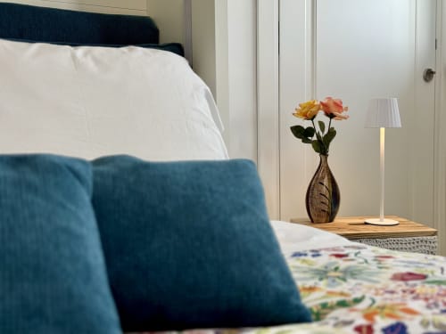 Camera elegante ad Aurora View Resort con cuscini blu, biancheria bianca e comodino con fiori freschi e lampada