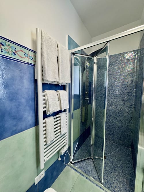 Bagno moderno con piastrelle blu e verdi, doccia aperta con mosaici, scaldarottoli e asciugamani bianchi