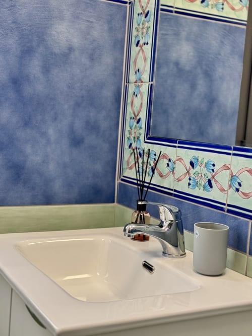 Moderno lavabo da bagno con rubinetto cromato, tazza in ceramica bianca, diffusore decorativo e parete con piastrelle blu e bordo floreale