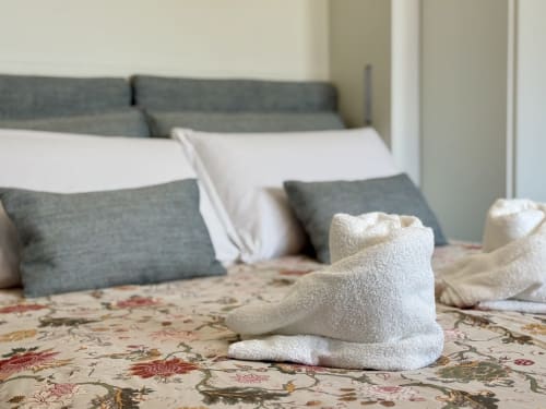 Asciugamani bianchi piegati su coperta floreale nella camera deluxe di Aurora View Resort con testata e cuscini grigi