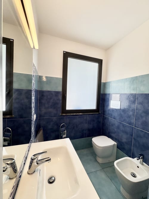 Bagno moderno dell'Aurora View Resort con doppio lavabo, toilette, bidet, piastrelle blu e verdi, specchio e illuminazione brillante