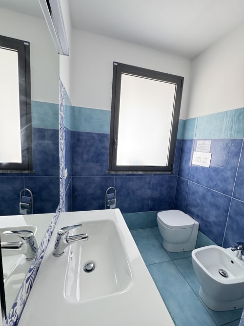 Bagno moderno di Aurora View Resort con doppio lavabo, toilette, bidet, piastrelle blu e azzurre, specchi e finestre