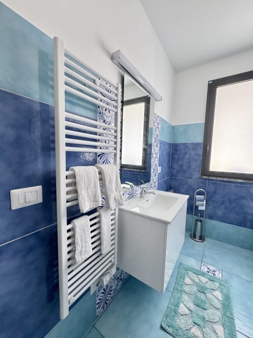 Bagno moderno presso Aurora View Resort con piastrelle blu, lavabo bianco, scaldasalviette e specchio