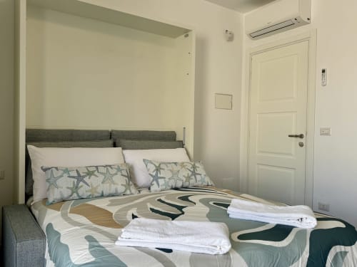 Camera da letto Aurora View Resort con letto rivestito in grigio, cuscini a forma di stella marina e biancheria a motivi in tonalità chiare e scure