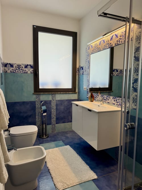 Bagno moderno dell'Aurora View Resort con pavimenti in piastrelle blu, lavabo bianco, accenti decorativi in piastrelle blu e oro, e