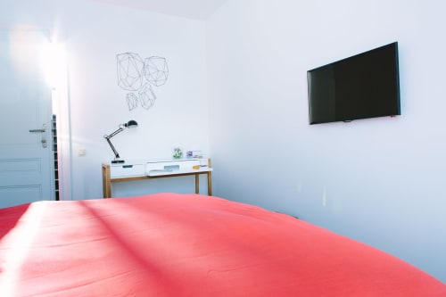 Chambre double moderne au B&B Place Jourdan Bruxelles avec lit rouge, TV murale, bureau avec lampe et art géométrique