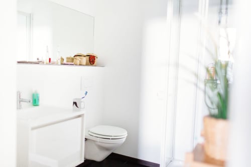 Salle de bain moderne et épurée avec toilettes blanches, lavabo, miroir et rangements dans une chambre double d'une maison d'hôtes bruxelloise