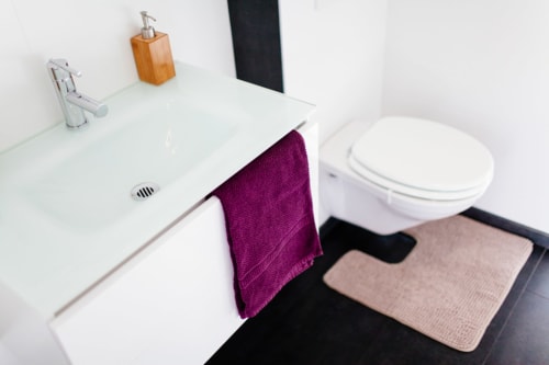 Salle de bains moderne du B&B Place Jourdan Bruxelles avec lavabo blanc, toilettes, serviette violette et tapis de bain beige