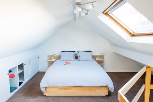 Chambre lumineuse avec verrière à la mansarde du B&B Place Jourdan Bruxelles, lit en bois, linge de lit bleu et rangements.