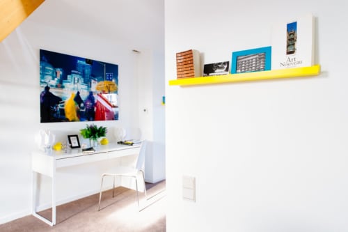 Studio moderne au B&B Place Jourdan Bruxelles avec bureau blanc, étagère jaune et œuvres d'art urbaines colorées sur murs blancs