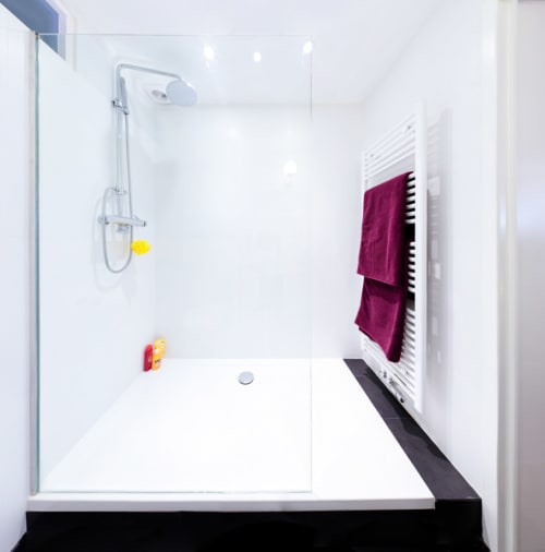 Salle de bain moderne avec pluie de douche et serviettes bordeaux sur porte-serviettes chauffant à la B&B Place Jourdan, Bruxelles