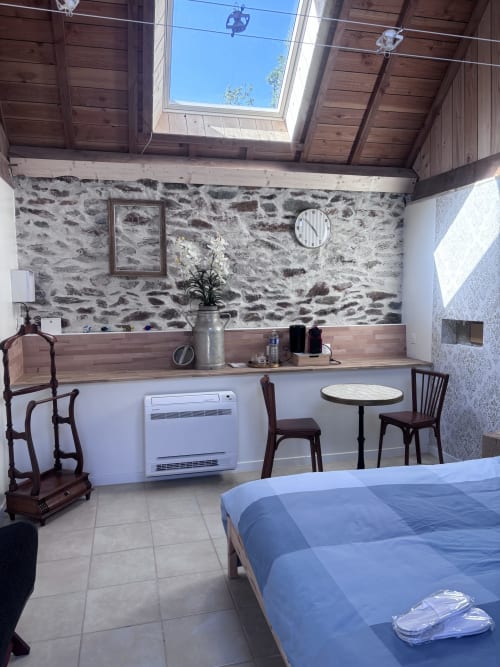 Chambre du gîte Lannedern avec murs en pierre, plafond en bois, lit, bureau et petite table sous des puits de lumière