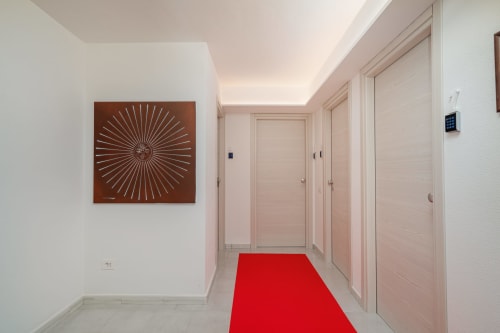 Corridoio moderno di Short Let's Olbia con tappeto rosso, opera d'arte con motivo solare e porte rosa pallido