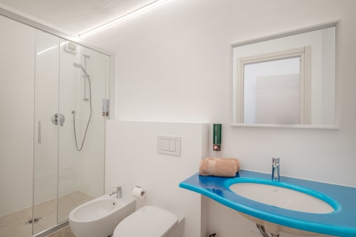 Bagno moderno di Short Let's Olbia con vanity blu, doccia aperta, WC e ampia finestra