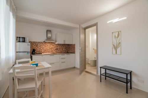 Modern kitchen and dining area with white cabinetry, brick backsplash, table, and bathroom access at Short Let's Olbia
