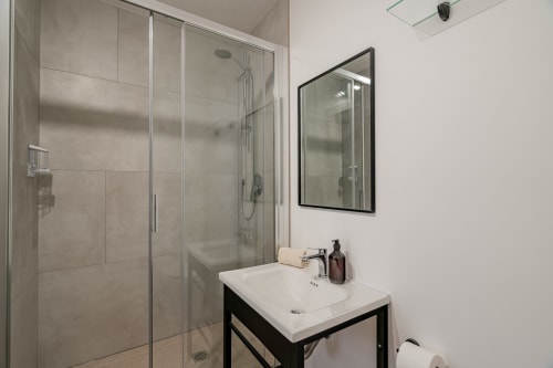 Modern bathroom at Short Let's Olbia hotel with glass shower enclosure, white sink, and black-framed mirror