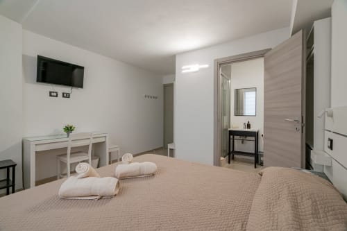 Modern hotel room at Short Let's Olbia with queen bed, flat-screen TV, desk, and ensuite bathroom in Olbia, Italy