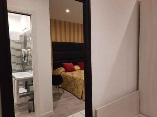 Camera Maritza Guest House Roma con bagno ensuite, biancheria dorata, cuscini rossi e parete a righe