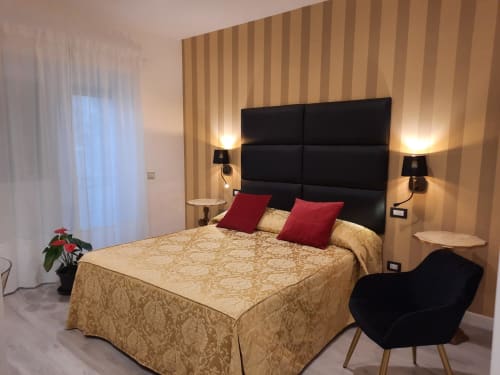 Camera elegante alla Maritza Guest House di Roma con testata nera, biancheria beige a motivi, cuscini rossi e arredi a righe calde