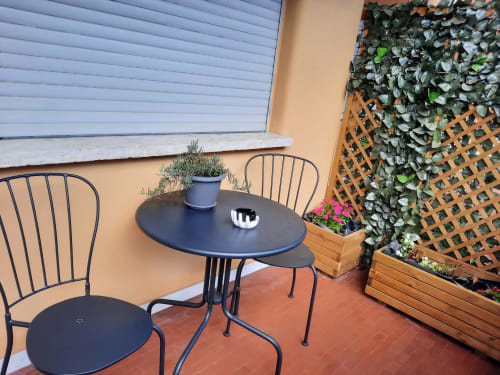 Accogliente balcone della Maritza Guest House Roma con sedie in metallo nero, tavolo rotondo, piante in vaso e traliccio ricoperto d'edera