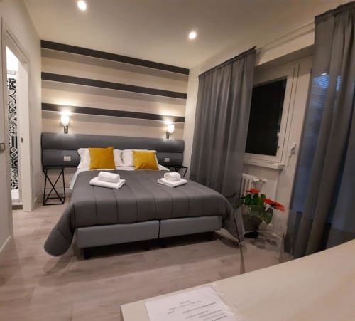 Camera moderna a Maritza Guest House Roma con parete a righe, letto grigio, cuscini gialli e vista sulla città dalle finestre