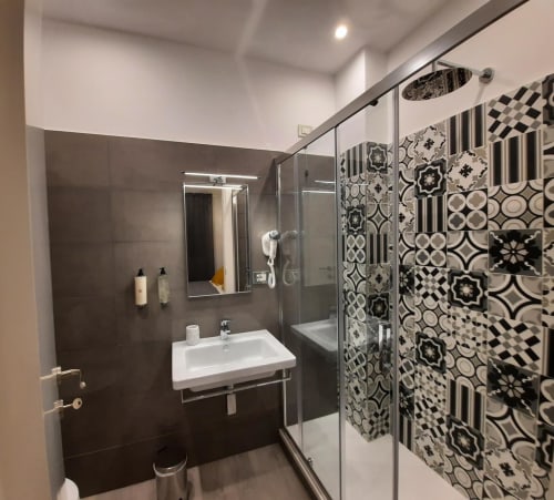 Bagno moderno presso la Maritza Guest House Roma con piastrelle nere, lavandino bianco, box doccia con motivi decorativi, e