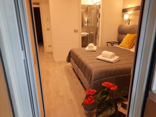 Camera Baldo 2 presso la Maritza Guest House Roma con letto marrone, asciugamani bianchi, fiori rossi e bagno privato