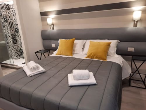 Camera moderna alla Maritza Guest House Roma con letto grigio, cuscini gialli e testiera a righe con applique da parete