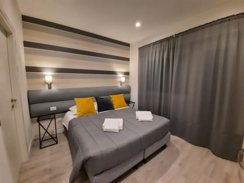 Camera moderna a Maritza Guest House Roma con parete a righe, letto grigio, cuscini gialli e tende con vista sulla città