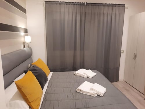 Camera moderna presso Maritza Guest House Roma con letto grigio, cuscini gialli e tende grigio scuro da pavimento a soffitto con vista su