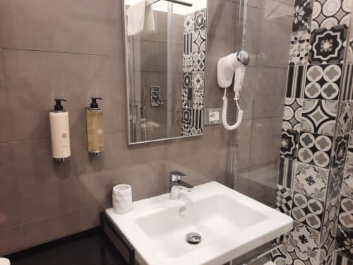 Bagno moderno nella Maritza Guest House Roma con lavabo bianco, accessori da parete e doccia con piastrelle bianche e nere