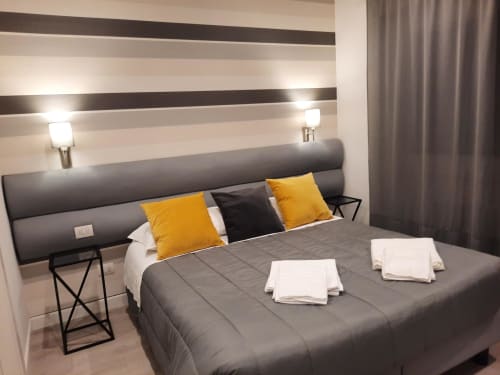 Camera moderna di Maritza Guest House Roma con letto grigio, cuscini gialli, testata a righe e vista sulla città