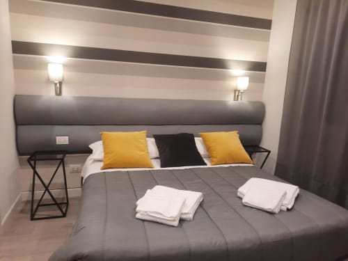 Camera moderna alla Maritza Guest House Roma con testata imbottita grigia, parete a righe, cuscini gialli e fresca