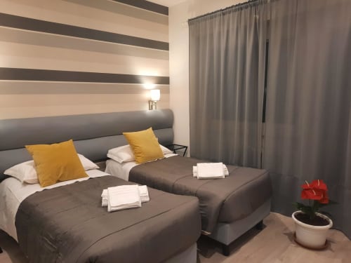 Camera doppia Baldo 2 della Maritza Guest House Roma con parete a righe, cuscini gialli e tende con vista sulla città
