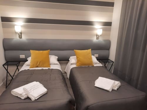 Camera gemella moderna a Maritza Guest House a Roma con testata imbottita grigia, parete a righe e cuscini gialli