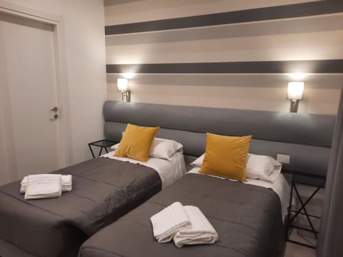 Camera doppia moderna presso Maritza Guest House Roma con parete a righe, testata grigia, cuscini gialli e servizi alberghieri