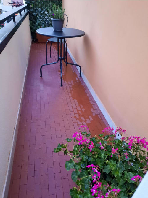 Balcone della Maritza Guest House Roma con fiori fucsia, tavolo rotondo nero e pavimento in cotto