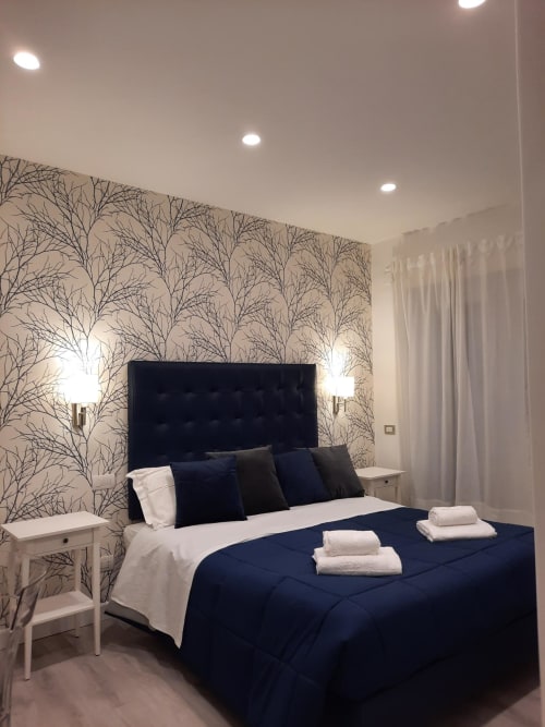 Camera moderna al Maritza Guest House Roma con testata blu navy, biancheria bianca, carta da parati a motivi floreali e illuminazione ambientale