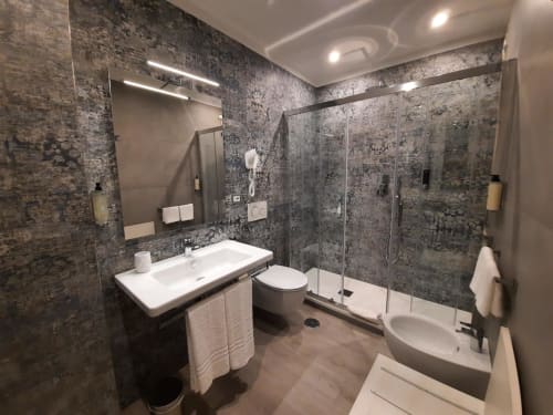 Moderno bagno a Maritza Guest House Roma con piastrelle scure, doppio lavabo, toilette e box doccia in vetro