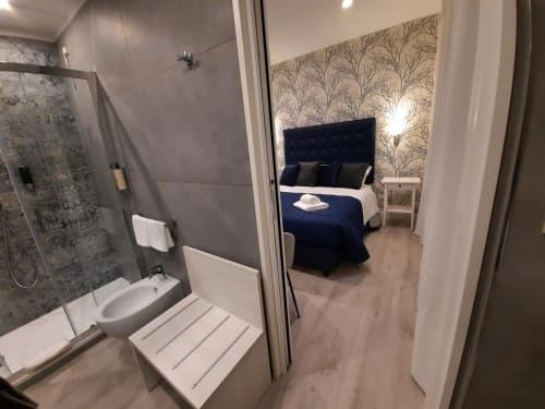 Camera da letto e bagno moderni nella Maritza Guest House Roma, con doccia, letto blu navy, carta da parati con alberi e vista sulla città