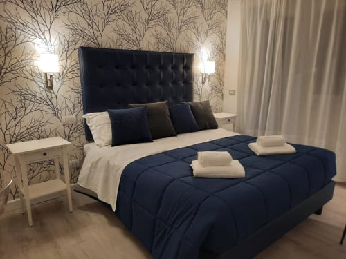 Camera moderna della Maritza Guest House a Roma con testiera trapuntata blu scuro, biancheria scura, lenzuola bianche e dettagli decorativi