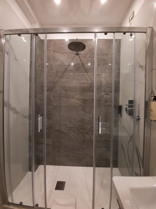 Doccia moderna con vetrate, rivestimento in marmo scuro e soffione pioggia nella camera di Maritza Guest House, Roma