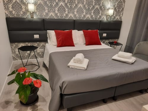 Camera Maritza Guest House Baldo 4 a Roma con letto queen size, cuscini rossi, carta da parati damasco e vista sulla città