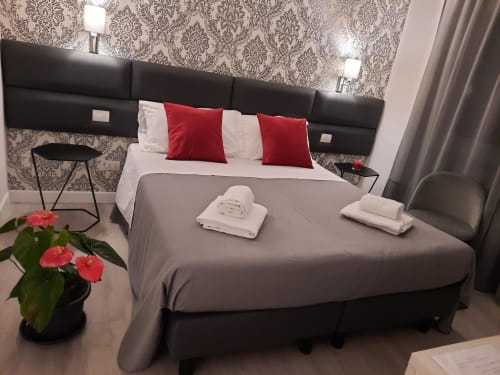 Camera Maritza Guest House Baldo 4 a Roma con testata nera moderna, cuscini rossi e bianchi, biancheria grigia e fiori freschi