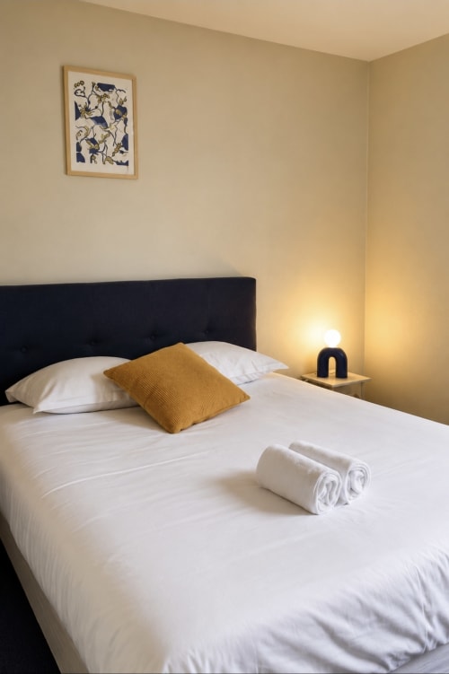 Chambre double moderne à l'hôtel Aux Genêts d'Or à Trévé avec tête de lit noire, literie blanche, coussin moutarde et ambiance chaleureuse