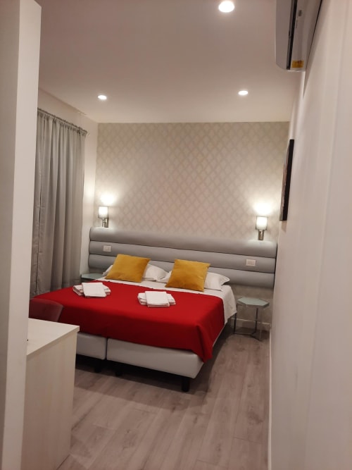 Camera moderna alla Maritza Guest House Roma con plaid rosso, cuscini gialli, testata grigia e vista sulla città