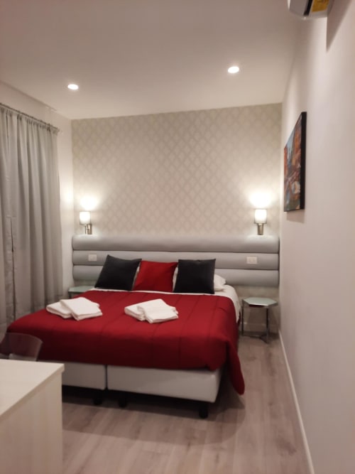 Camera moderna della Maritza Guest House Roma con letto rosso, testiera grigia, applique murali e vista sulla città