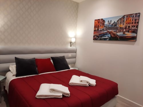 Camera moderna alla Maritza Guest House Roma con coperta rossa, testata grigia e arte paesaggistica italiana