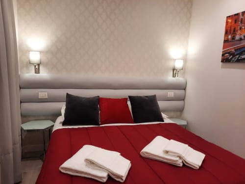Camera moderna a Maritza Guest House Roma con biancheria rossa, cuscini neri, testiera imbottita grigia e applique doppie